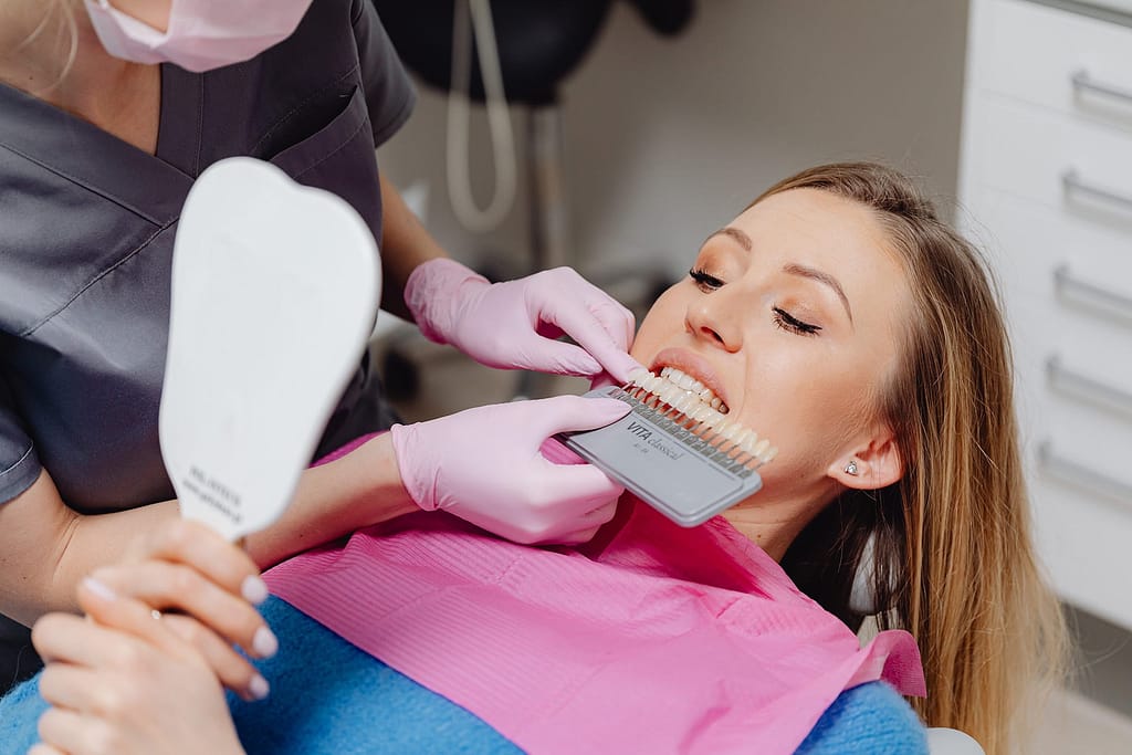 A woman undergoing a dental check-up with a shade guide to match teeth color in a dental clinic.