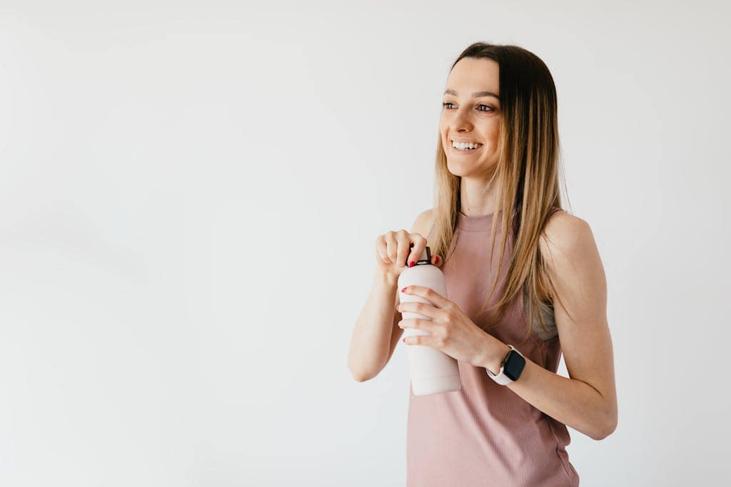 Cheerful young woman in casual attire opens a water bottle, showcasing a healthy lifestyle.