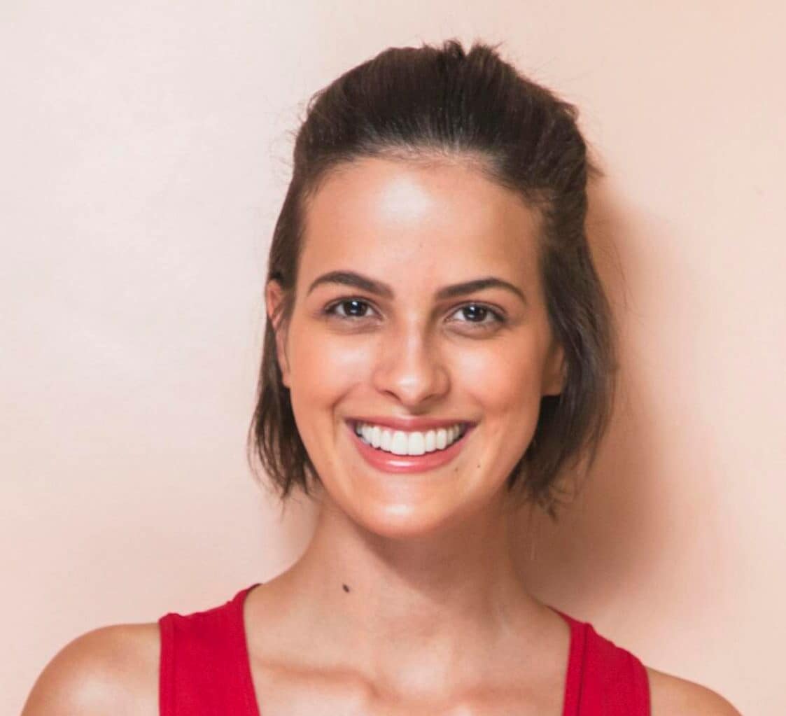 Portrait of a smiling woman wearing a red tank top, standing against a neutral background.