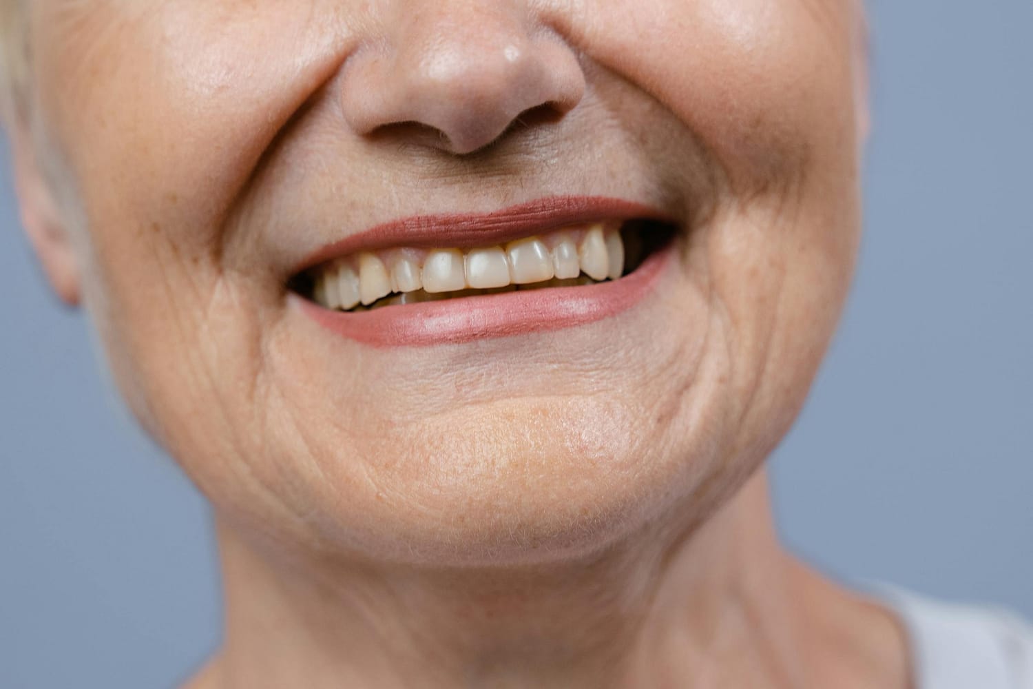 A detailed close-up of a senior woman's smile showcasing her natural teeth and wrinkles.