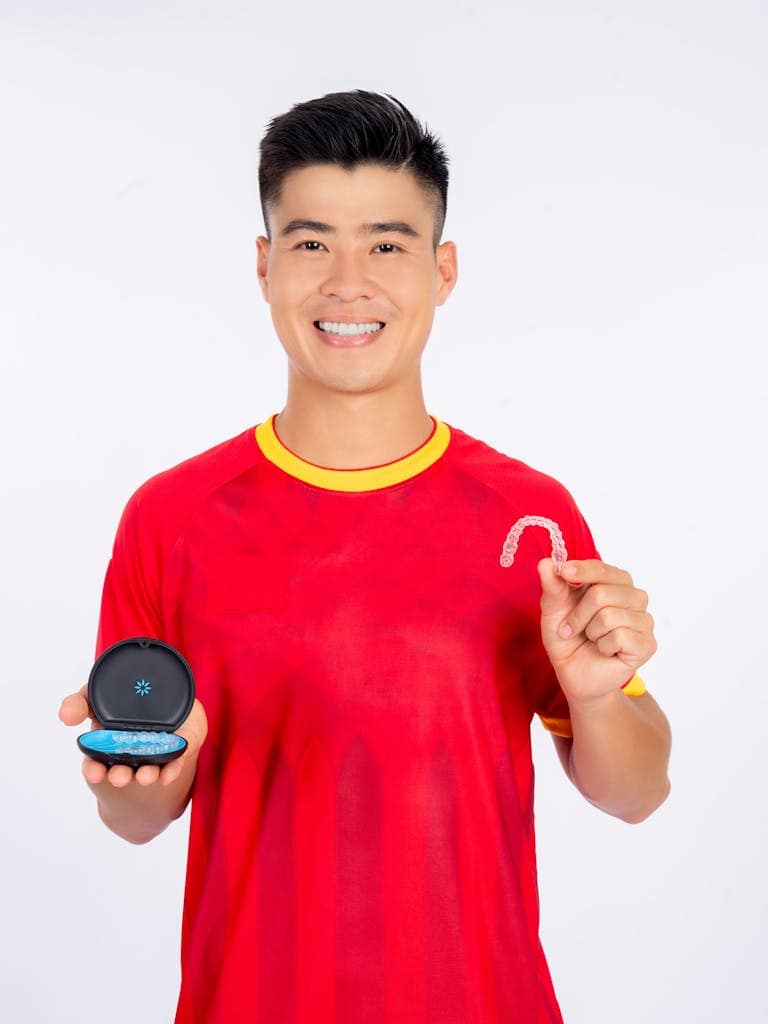 Happy man in red shirt holding a clear dental retainer and its case, showcasing dental care.