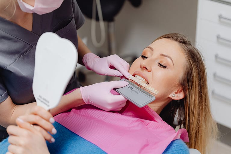 A woman undergoing a dental check-up with a shade guide to match teeth color in a dental clinic.
