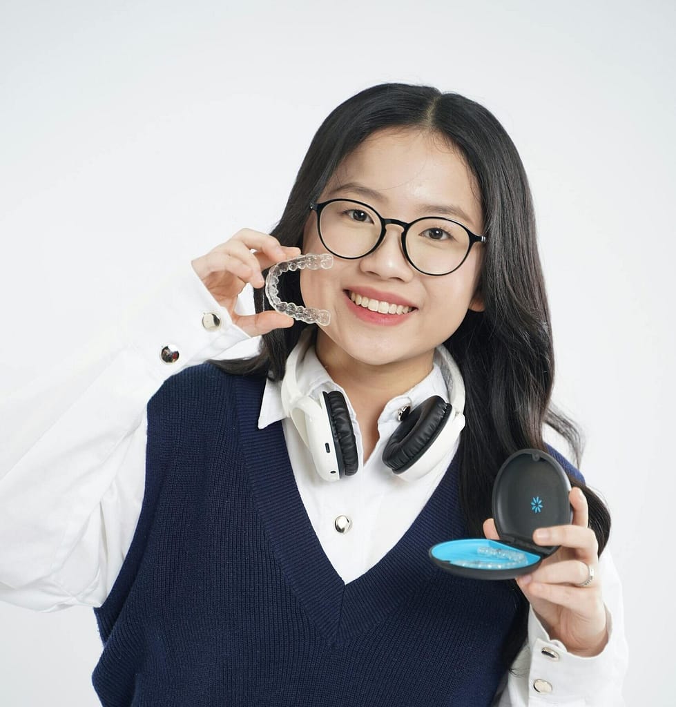 Happy woman displaying clear aligners with headphones around neck